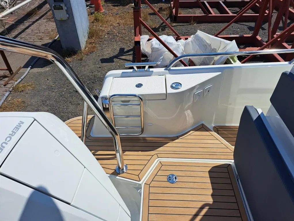 View of a boat's rear deck with polished stainless steel railing, wood flooring, and a white storage compartment.
